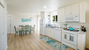 Una cocina moderna con armarios blancos, una estufa a gas, un microondas y un comedor con mesa y sillas.