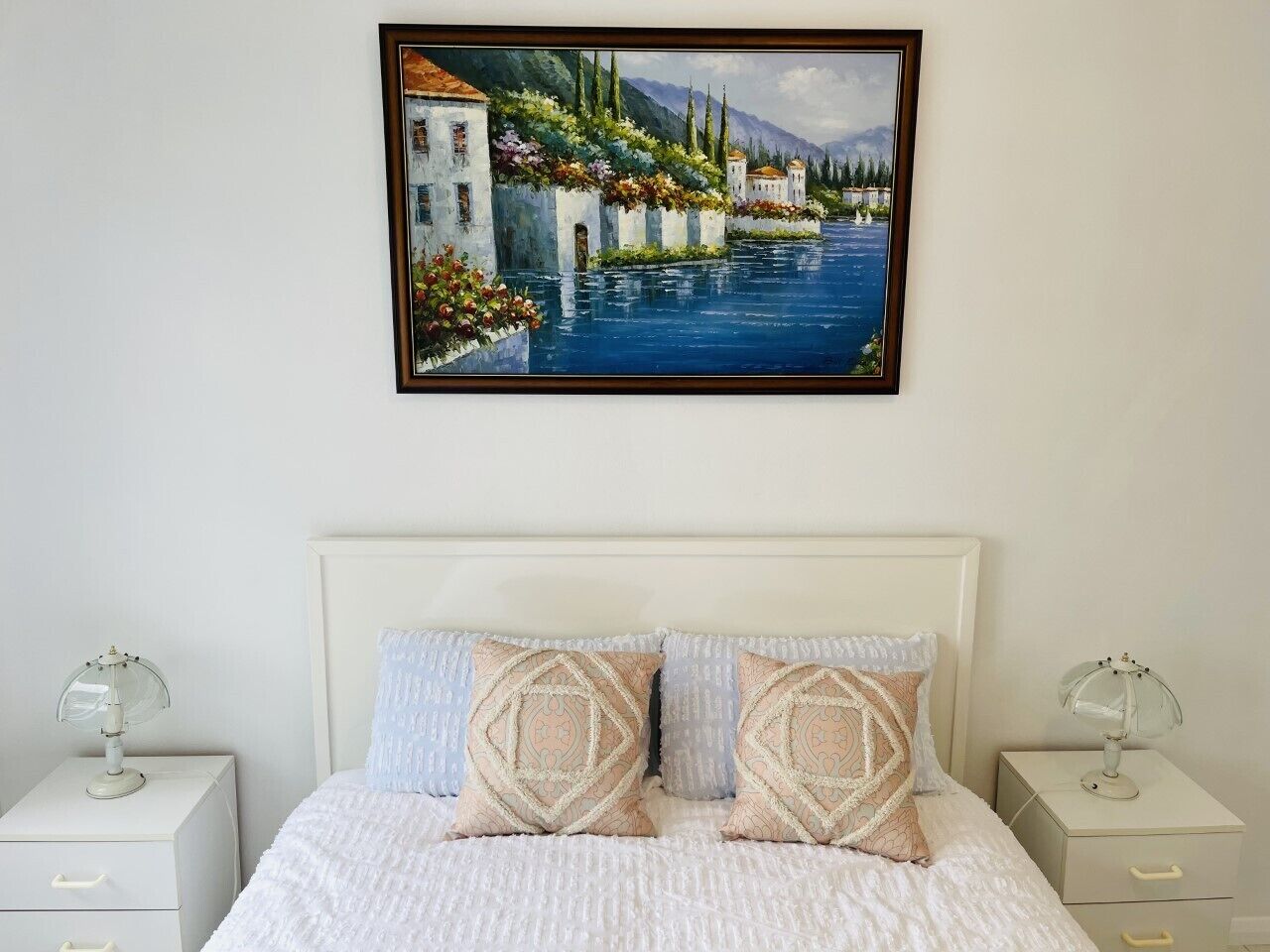 A bedroom with a bed, two bedside tables, and a painting above the bed.