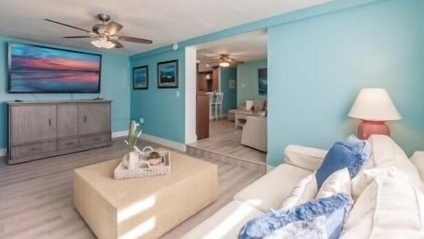 A living room with a sofa, a coffee table, and a TV. There is a ceiling fan and a lamp.