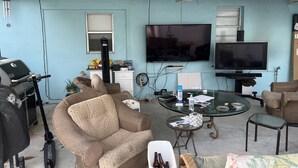 A living room with a ceiling fan, two TVs, a grill, and wicker furniture.