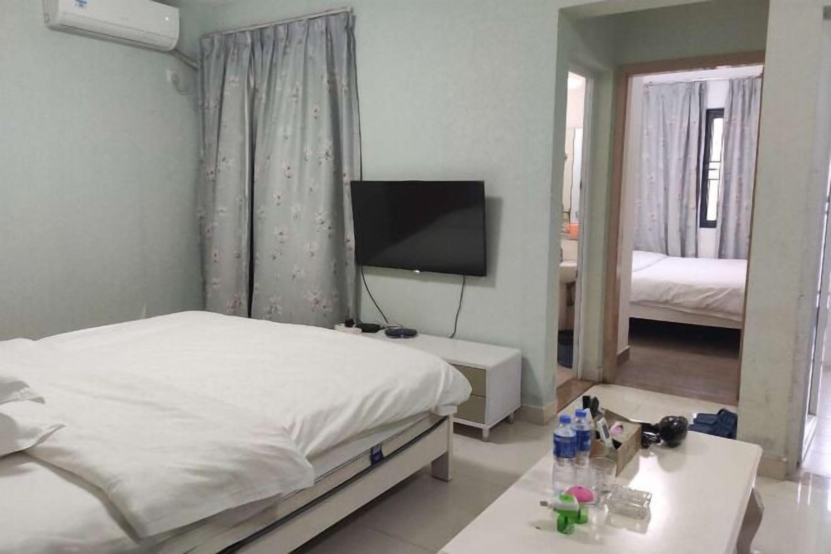 A hotel room with a bed, a TV mounted on the wall, a small bedside table, and a desk with various items.
