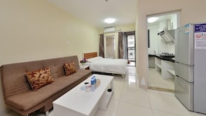 A hotel room with a sofa, a bed, a white coffee table, and a kitchenette area. - Tiantianhui Apartment Hotel (Shenzhen)