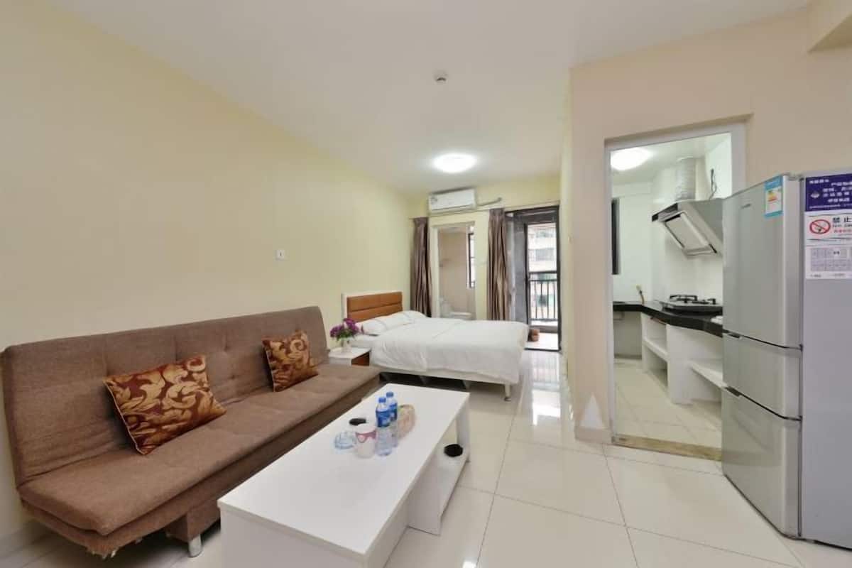 Habitación de hotel con sofá, cama, una mesita de centro blanca y una zona de kitchenette.