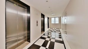 A hallway with a checkered floor, elevators, and a plain wall with a small sign. - Tiantianhui Apartment Hotel (Shenzhen)