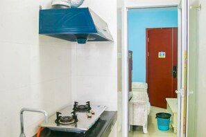 Une petite cuisine équipée d’une cuisinière à gaz, d’une hotte d’extraction bleue et d’un mur recouvert de carreaux blancs.
