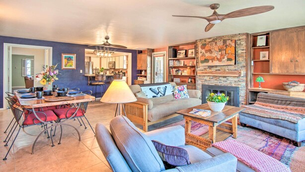 A living room with a sofa, armchairs, a coffee table, and a dining table with chairs. There is a fireplace, a ceiling fan, and a bookshelf with various items. - Tucson House w/ Private Pool: 5 Mi to Downtown! (Tucson)