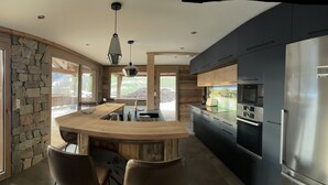 Una cocina moderna con una isla central, paredes de piedra y un refrigerador grande.