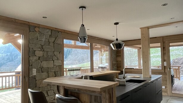Una cocina moderna con una pared de acento de piedra, ventanas amplias y una zona de bar con taburetes.