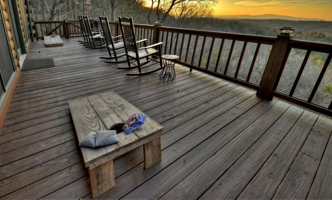 A wooden deck with a bench, chairs, and a table, overlooking a forested landscape.