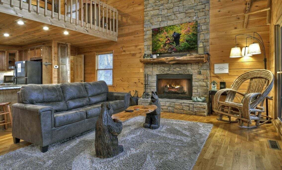 A cozy cabin interior with a stone fireplace, wooden walls, a sofa, and a dining table.