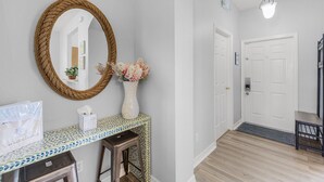 A hallway with a white door, a mirror, a vase with flowers, and a tiled console table.