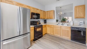 A modern kitchen with stainless steel appliances, wooden cabinets, and a light-colored floor.