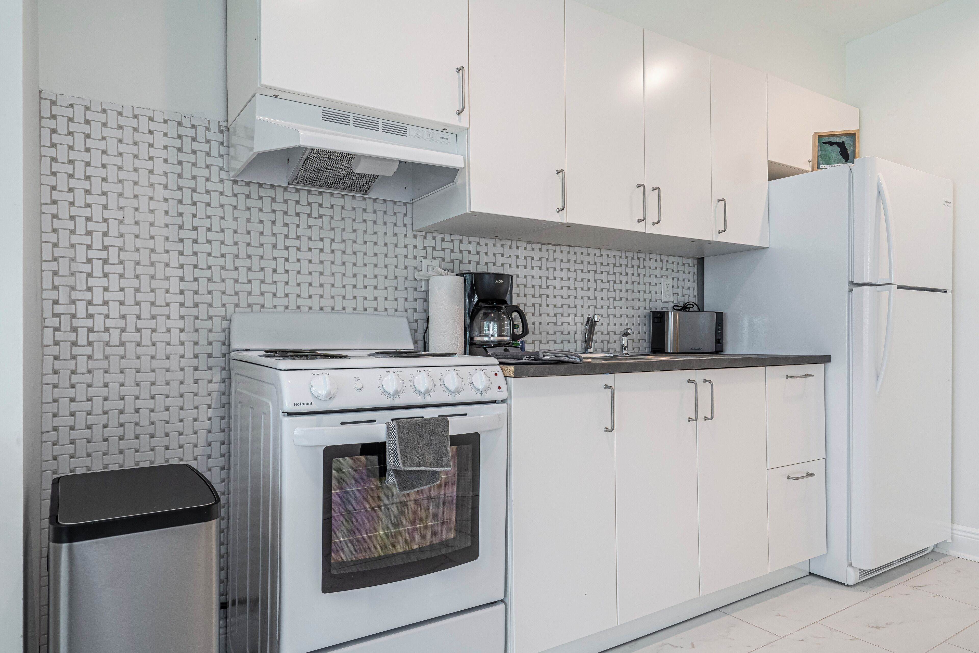 Una cucina moderna con mobili bianchi, un piano cottura in acciaio inossidabile e un frigorifero bianco.