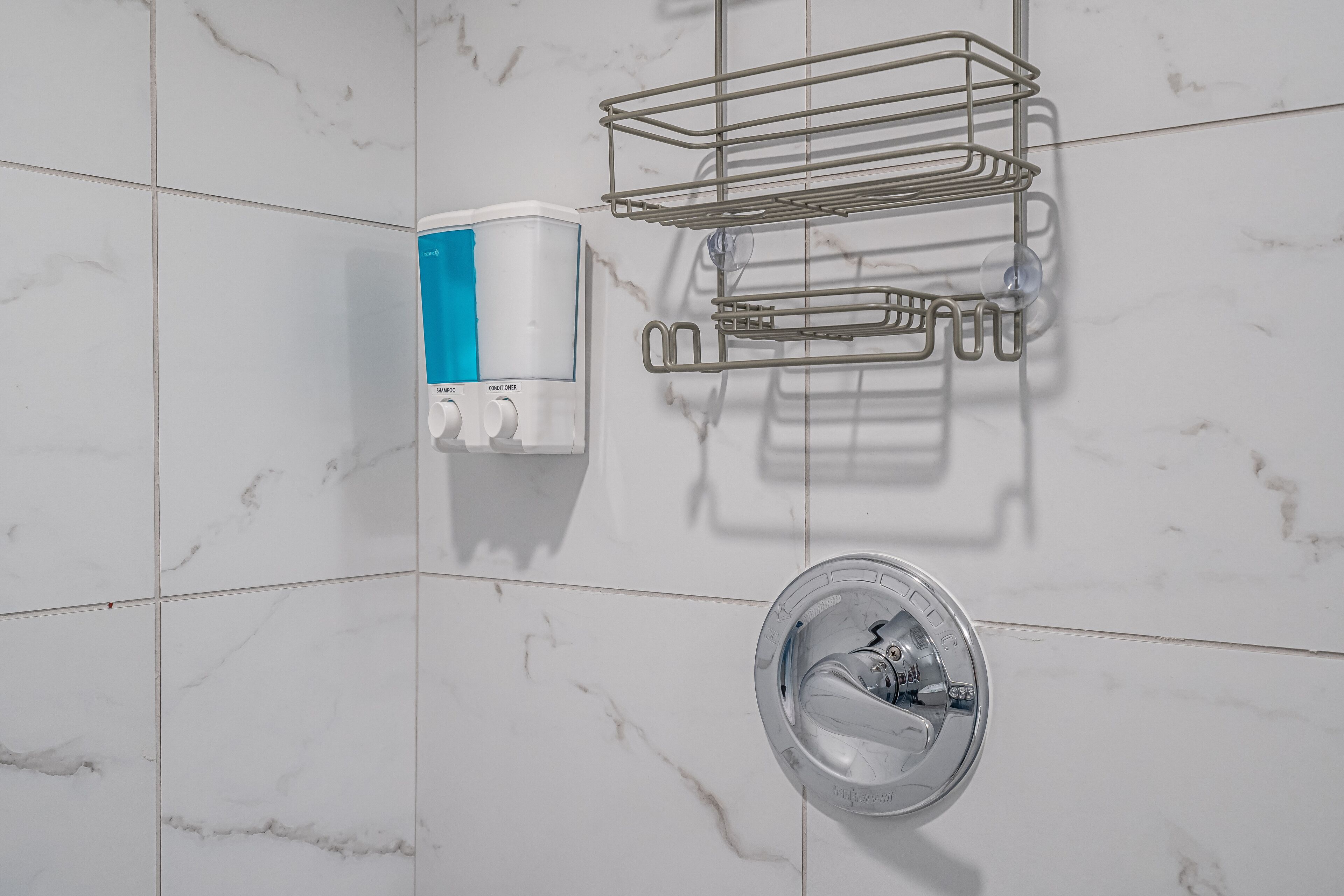 A bathroom with a marble wall, a soap dispenser, a metal towel rack, and a chrome sink.