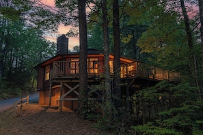 A cabin with a deck, surrounded by trees. - Country Cozy - Hot Tub with Mountain Views, Fireplace & Pac-Man Arcade (Gatlinburg)