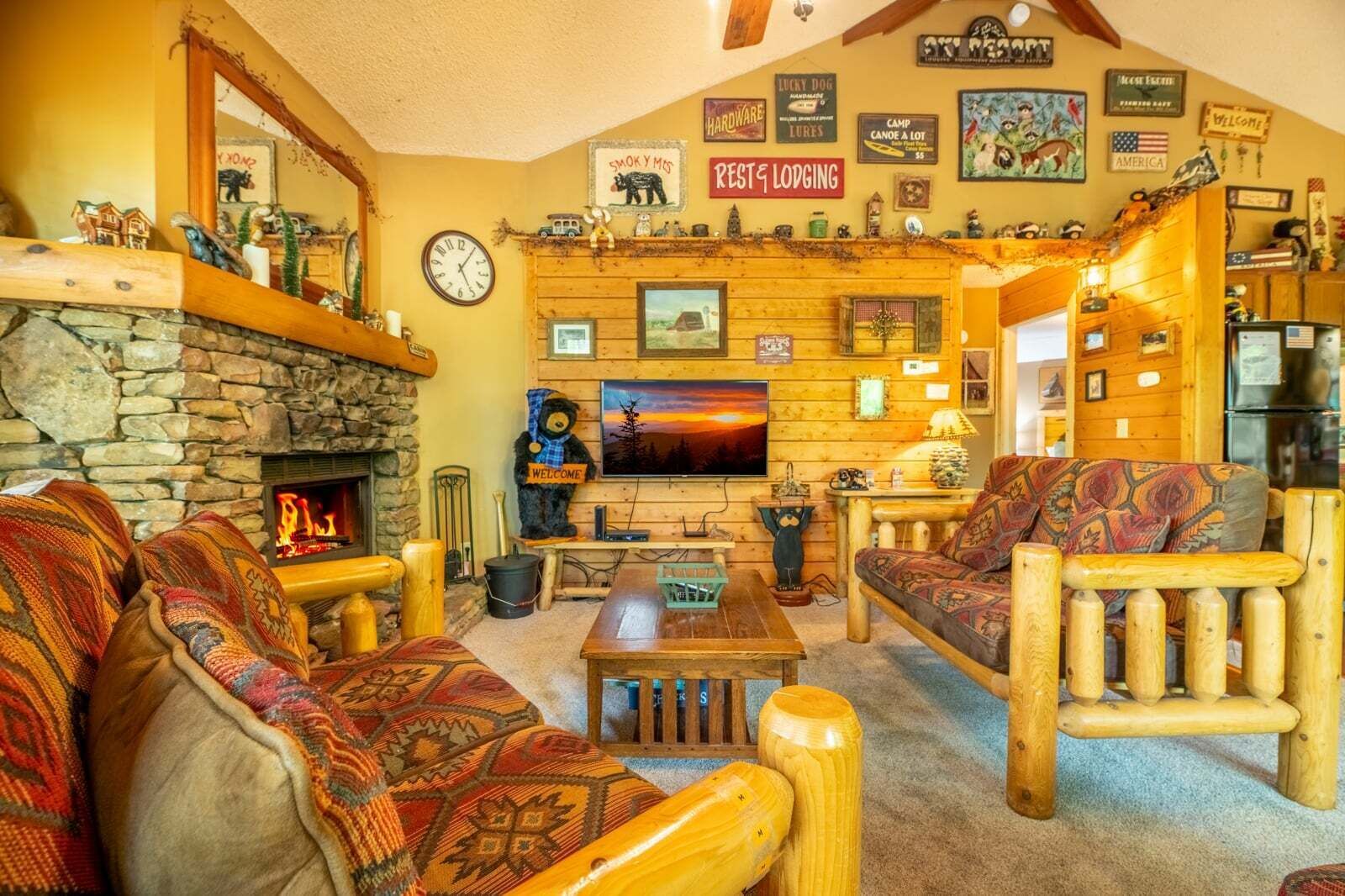 A cozy lodge interior with a stone fireplace, wooden furniture, a television, and various wall decorations.