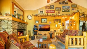 Ein gemütliches Blockhaus-Interieur mit Kamin aus Stein, Holzmöbeln, einem Fernseher und verschiedenen Wanddekorationen.