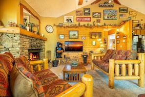 A cozy lodge interior with a stone fireplace, wooden furniture, a television, and various wall decorations.