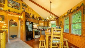 Ein Interieur einer Holzhütte mit Holzwänden, einer Küche mit Kühlschrank, Herd und einem Essbereich mit Holzsesseln.