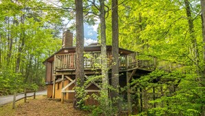 Eine Holzhütte mit einer Holzterrasse und Schornstein, umgeben von dichtem Wald.