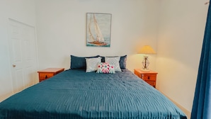 Ein Schlafzimmer mit einem großen Bett, zwei Nachttischen, einer Lampe und einem Gemälde mit einem Segelboot an der Wand.