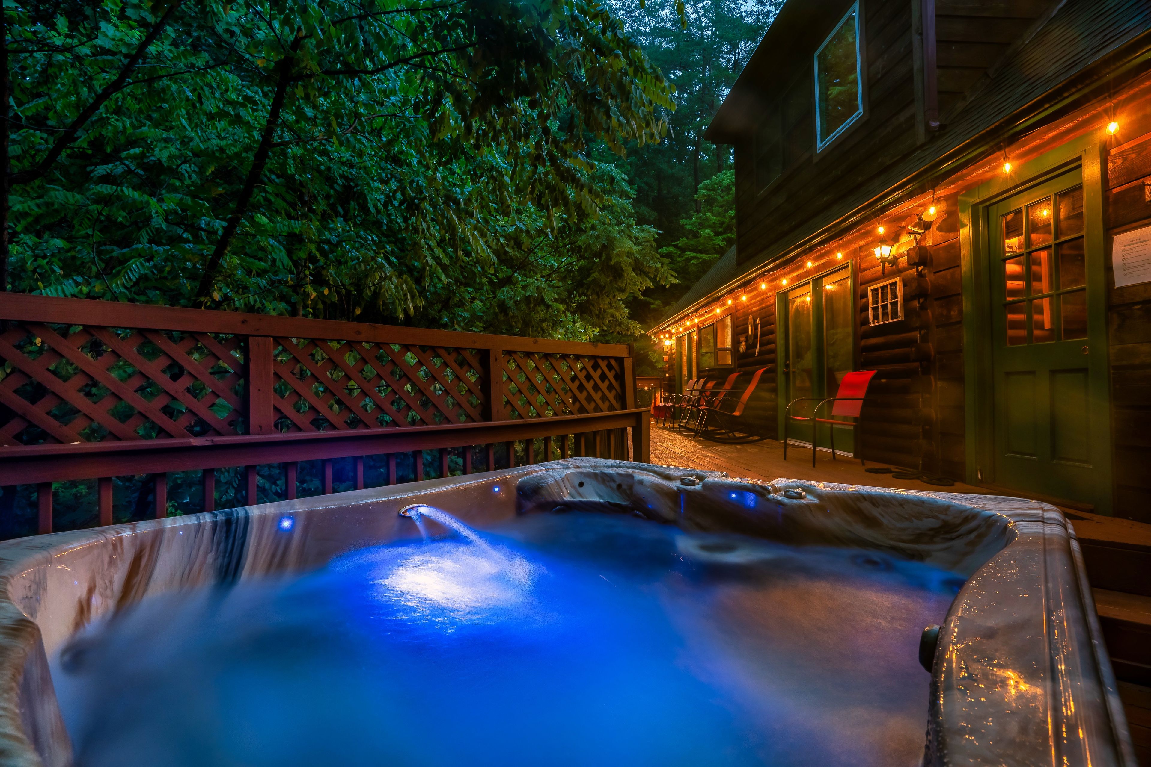 Un jacuzzi con una terraza de madera y un edificio de madera con luces colgantes al fondo.
