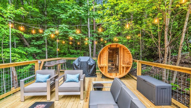 A wooden deck with outdoor seating, a sauna, and string lights in a forested area. - Newly Renovated! NEW deck & SAUNA! 3 King Bedrooms! Hot tub/Arcade. Free tickets (Sevierville)