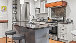 A modern kitchen with a central island, stainless steel appliances, and a wooden accent above the stove. - Luxury King Suite- Mountain Views/ 2 Balconies/Pool/Hot tub (Canmore)