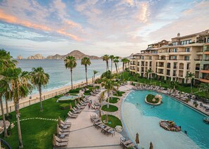 A resort with a pool, palm trees, and a view of the ocean. - Comfortable Beachfront Resort Two Bedroom with Upscale Furnishings and Personal Concierge Services (Cabo San Lucas)