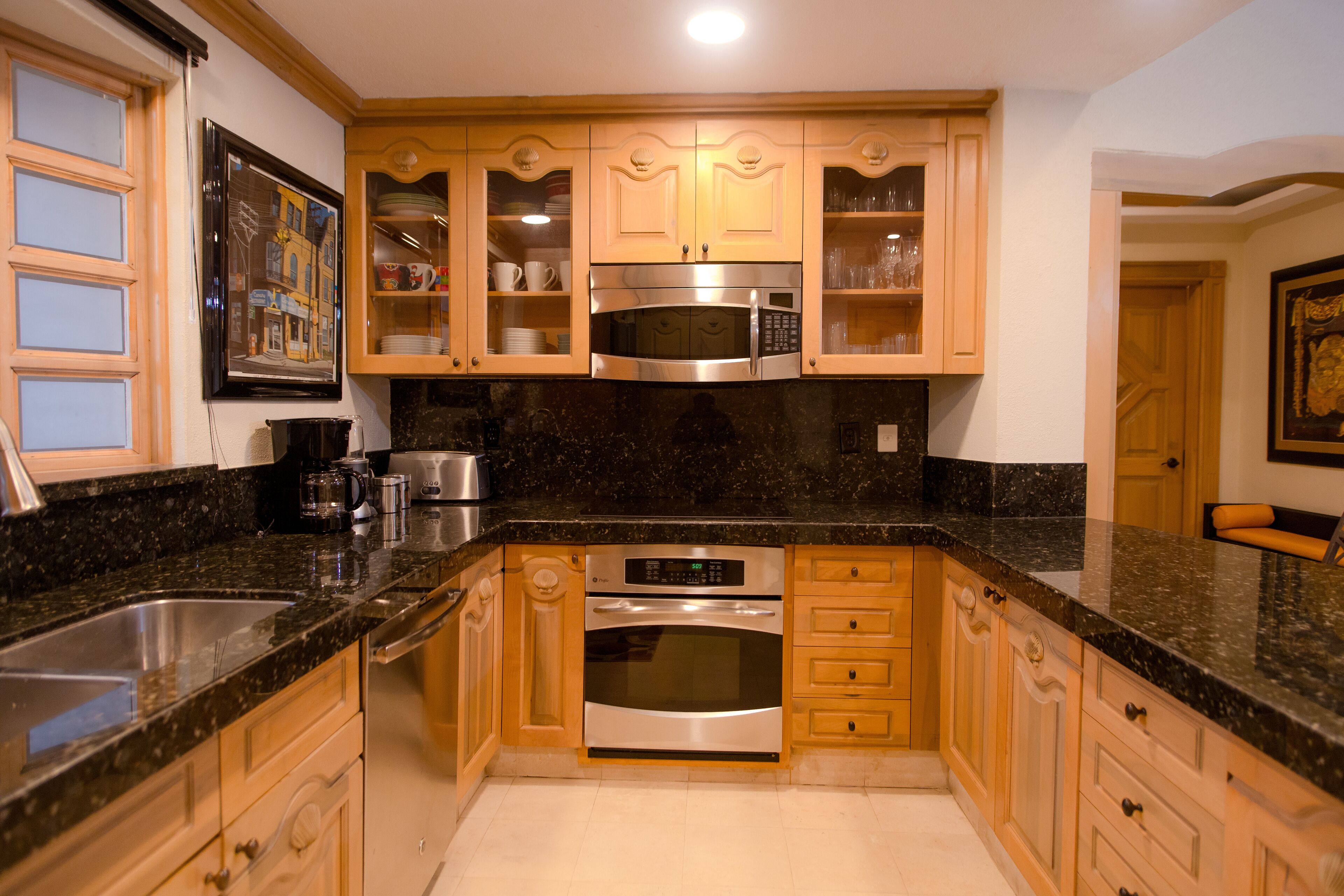 A kitchen with wooden cabinets, a stainless steel microwave, an oven, and a sink.