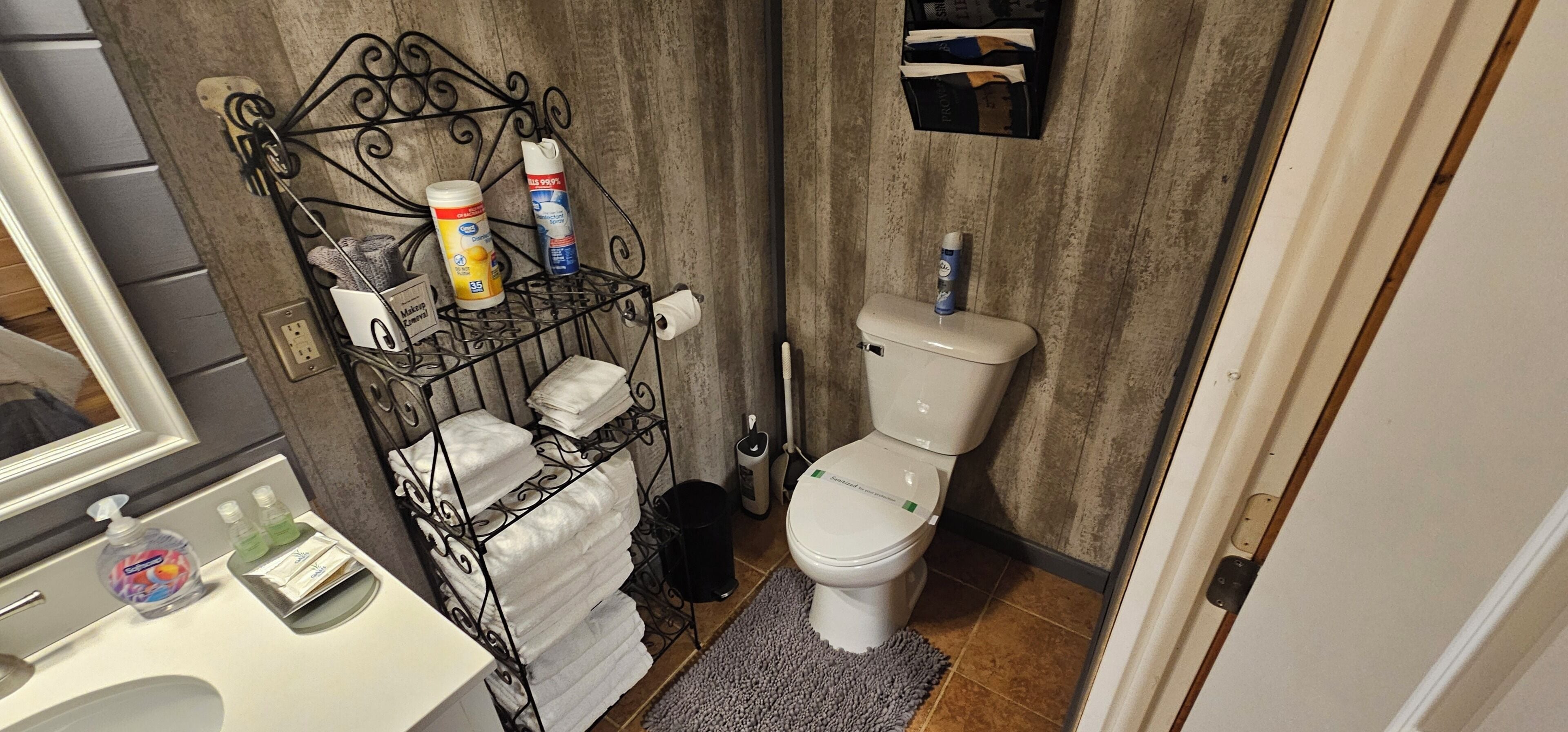A compact bathroom with a toilet, a metal rack with toiletries, and a small sink.