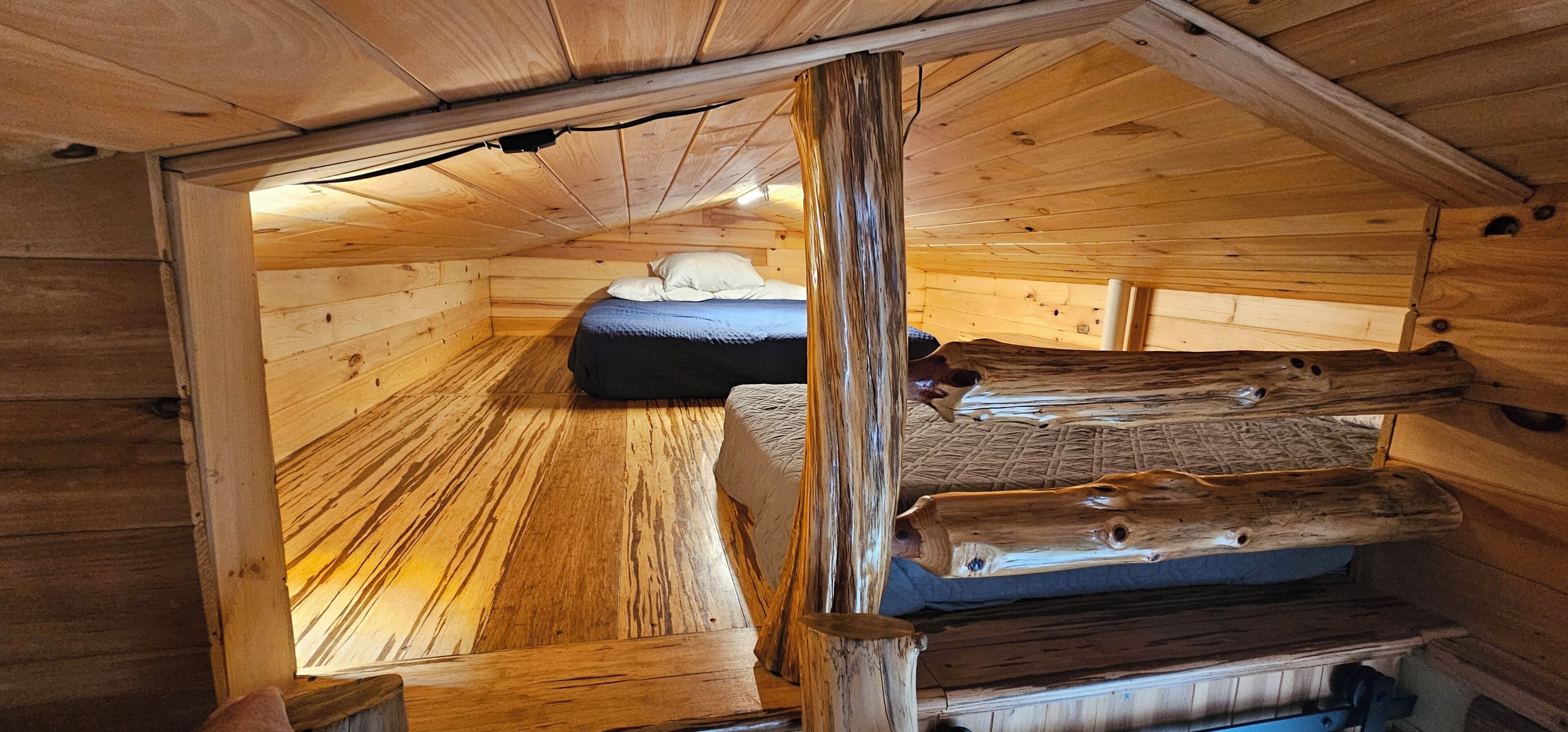 A wooden cabin with a loft bed, a small table, and a bench.