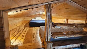 A wooden cabin with a loft bed, a small table, and a bench.