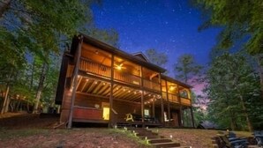 Una baita di legno a due piani con un balcone, immersa tra gli alberi sotto un cielo stellato.