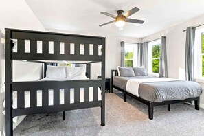 A bedroom with a bunk bed, a single bed, a ceiling fan, and a window with curtains.