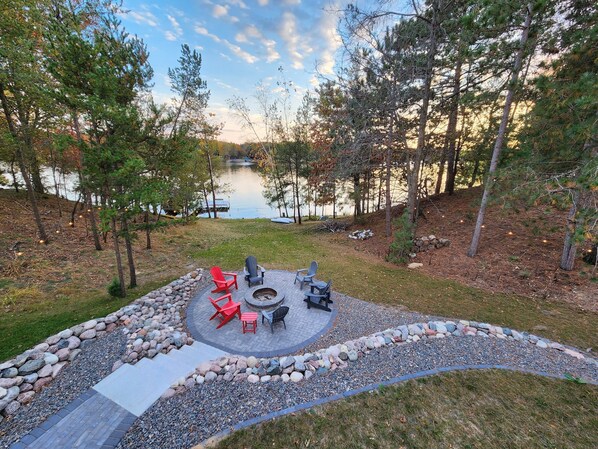 A circular outdoor seating area with a fire pit, surrounded by a stone border and a gravel path leading to it.