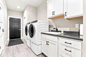 A laundry room with a washing machine and dryer, a sink with a faucet, and a countertop with a soap dispenser.
