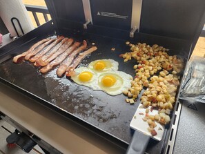 Ontbijt wordt bereid op een bakplaat, met baconreepjes, gebakken eieren en blokjes aardappels.