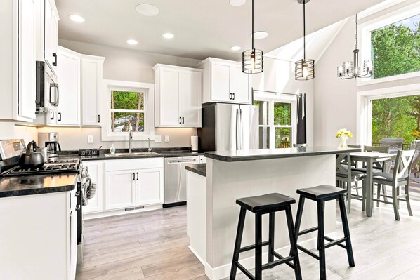 A modern kitchen with white cabinetry, a central island with stools, and a view of greenery outside.