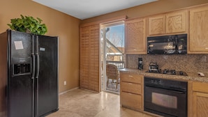 A kitchen with a black refrigerator, wooden cabinets, a microwave, and a stove. - Bear Snugglin - Close to Slopes, Hot Tub, Deck, Barbecue (Big Bear Lake)