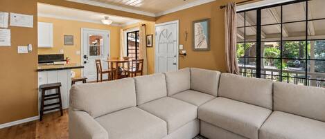 A living room with a sectional sofa, a dining area with a table and chairs, a kitchen with cabinets, and a ceiling fan.