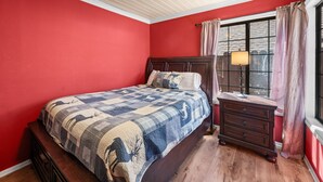 Een slaapkamer met een groot bed, een nachtkastje, een lamp en een raam met gordijnen.