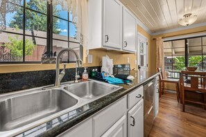 A kitchen with a double sink, a window with lace curtains, and a view of the outdoors.