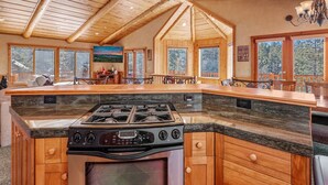 Een ruime keuken met een groot eiland, houten kastjes en een hoog plafond met zichtbare balken.