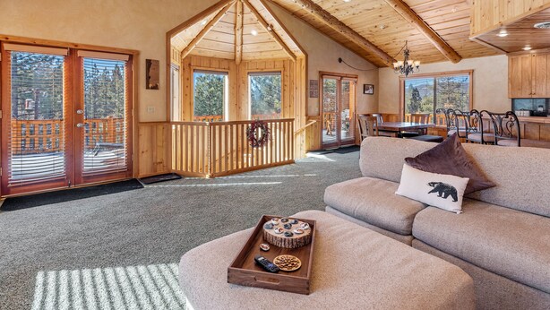 Een gezellig interieur van een chalet met een houten plafond, een eethoek en een groot raam met uitzicht op een terras.