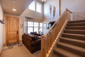 A spacious living area with a wooden staircase, a brown leather sofa, and a large window providing natural light.