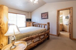A bedroom with a wooden bed frame, a bedside lamp, a television, and a framed picture on the wall.