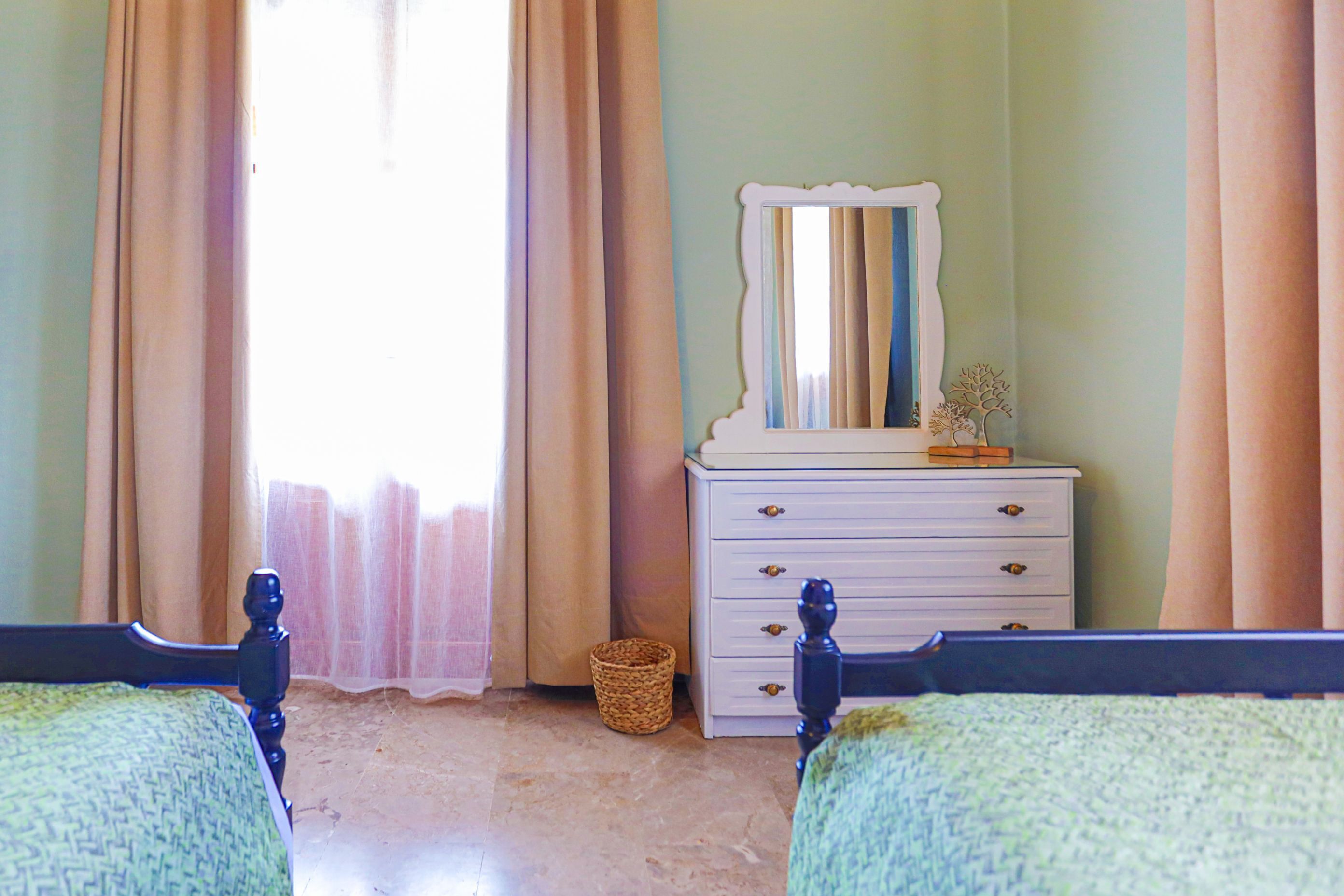 A bedroom with two beds, a dresser, a mirror, and a window with curtains.