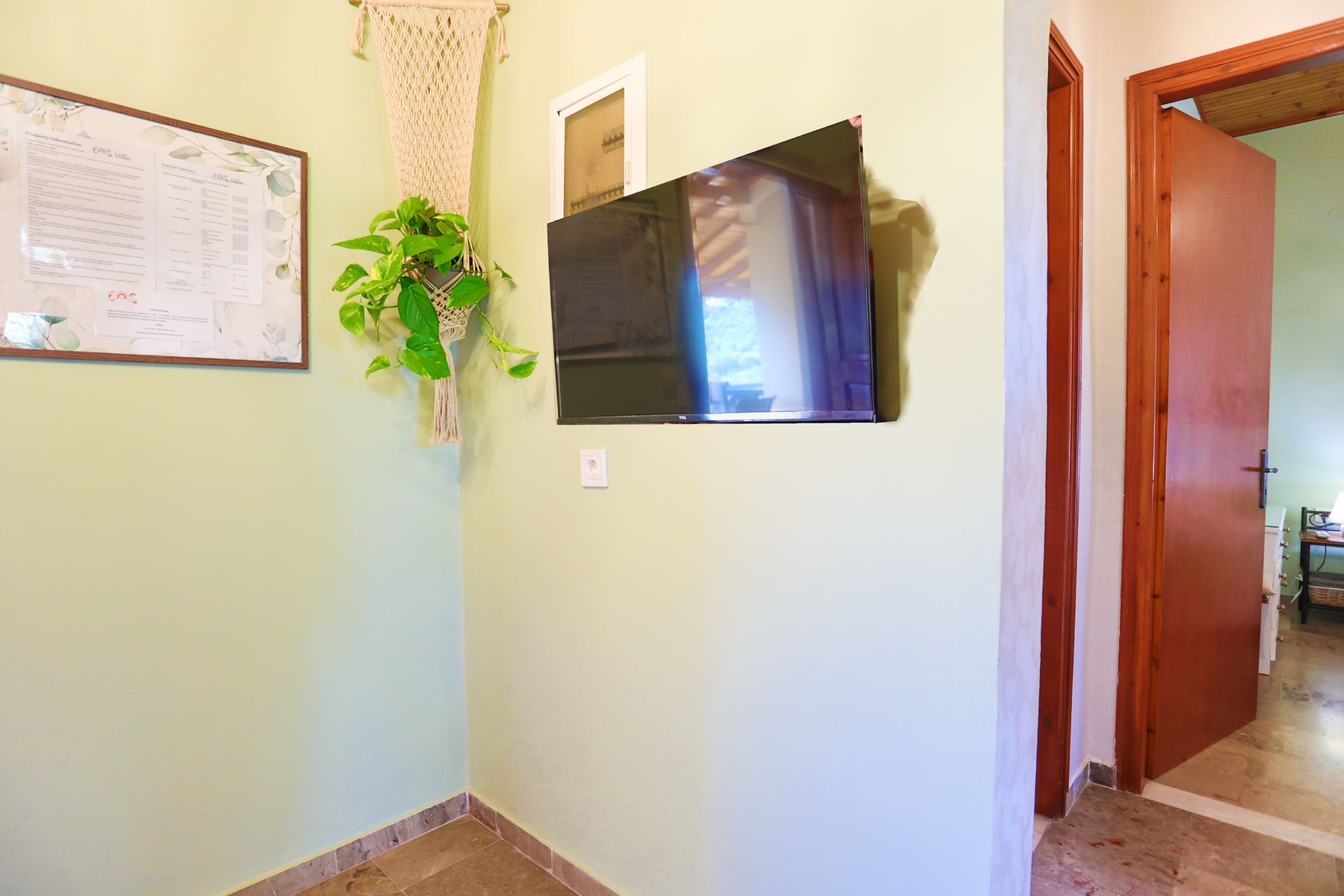Un pasillo con un tablón de anuncios enmarcado, una planta en maceta y una puerta que da a otra habitación.
