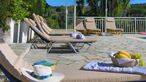 A poolside area with lounge chairs, umbrellas, and a basket of fruit.
